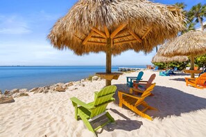 Een strand met rieten parasols, kleurrijke Adirondack-stoelen en uitzicht op de oceaan.