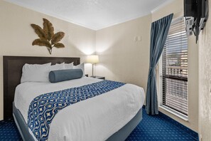 Ein Hotelzimmer mit einem großen Bett, einer Wandpflanze, einem Fenster mit Jalousien und einem Deckenventilator.