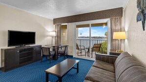A hotel room with a flat-screen TV, a dining table with chairs, a sofa, a balcony with a view of the city, and a patterned ceiling. - Partial Bay Views & Pool 1BR (Tampa)