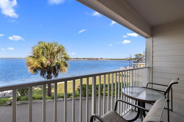 A balcony with a view of the water, a palm tree, and a table with chairs.