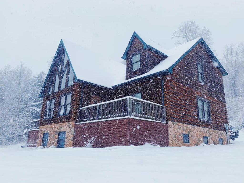 Een groot, meerlaags houten huis met een stenen fundering, omgeven door sneeuw.