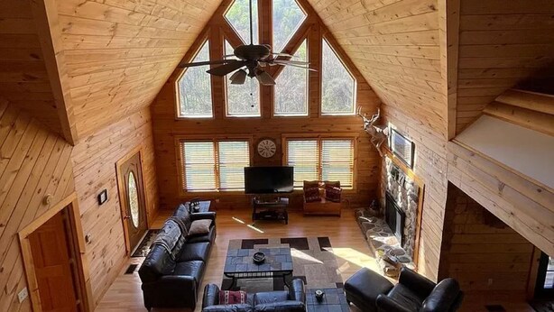 A spacious wooden cabin with a high ceiling, a fireplace, a television, and a cozy seating area.