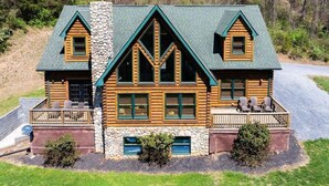 A log cabin with a stone chimney, multiple windows, and a porch with outdoor seating.
