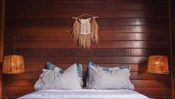 A bed with a blue blanket, two pillows, and a woven wall hanging. - Nomades beach - Adventure Hostels (Florianópolis)
