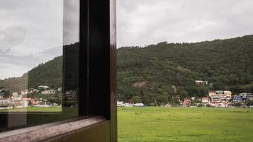 Une vue à travers une fenêtre, avec le reflet d’un champ verdoyant et d’une colline parsemée de bâtiments.
