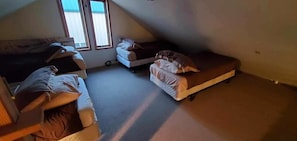 Un pequeño y tenuemente iluminado cuarto de ático con dos literas y una cama individual.
