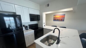 Una cocina moderna con armarios blancos, un refrigerador negro, una estufa y un microondas. Hay un lavamanos con grifo, un cuadro en la pared y una pequeña isla con encimera.