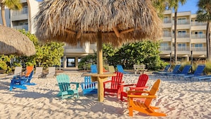 Un área de playa con sillas Adirondack de colores y un paraguas de paja.