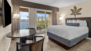 Una camera d'albergo con un letto, un tavolo e delle sedie, un balcone con vista sulle case e una pianta appesa al muro.