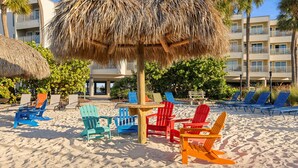 Un área de playa con sillas Adirondack de colores y un paraguas de paja.