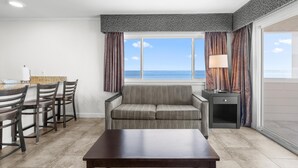 A room with a dining area, a sofa, and a view of the ocean.