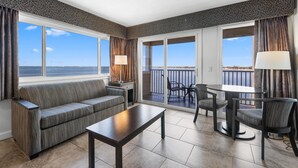 Una sala de estar moderna con sofá, mesa de centro y comedor con sillas y mesa. Amplias ventanas ofrecen vista al mar.