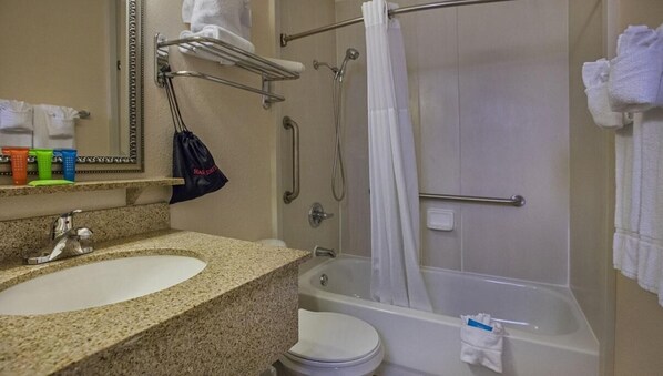 Une salle de bain avec un lavabo surmonté d’un plan de travail en granit, un miroir, une douche avec une porte en verre et un porte-serviettes.