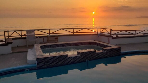 A pool area with a view of the sunset over the ocean.