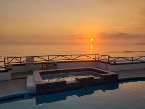 A pool area with a view of the sunset over the ocean.