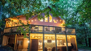 A two-story wooden cabin with a balcony, string lights, and a visible interior with a bed and seating area. - Blue Ridge Bliss 9BR/6BA: 2 Homes Across the Street from each other! Sleeps 24 (Wintergreen Resort)