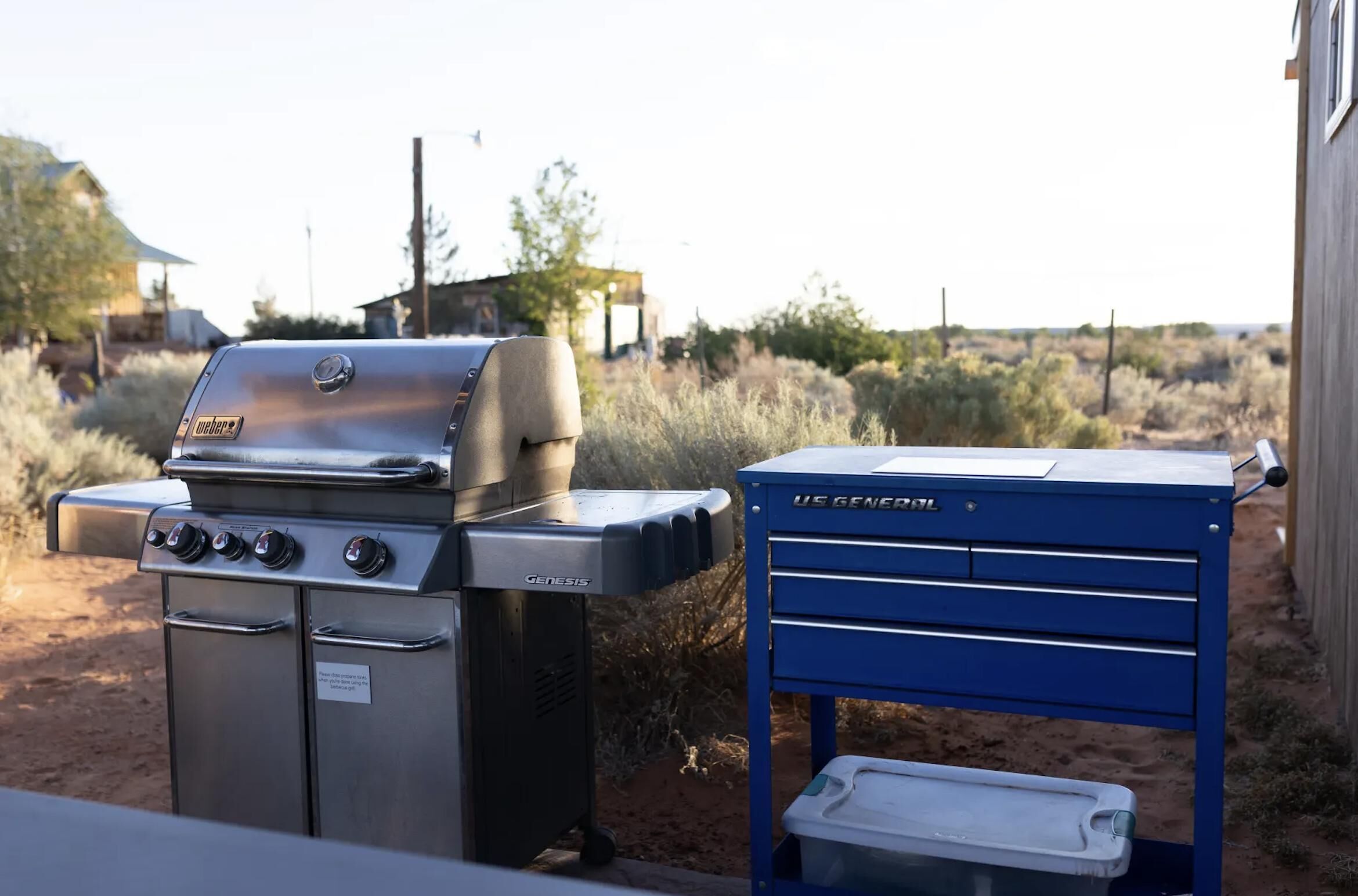 A Weber Genesis gas grill and a US GENCOIL blue tool chest outdoors.