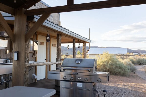 A covered outdoor area with a stainless steel grill, wooden beams, and a view of the desert landscape. - Glamp Tent b/w Zion & Bryce, Outdoor Shower & Wifi (Fredonia)
