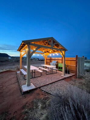 A covered outdoor seating area with picnic tables and string lights. - Glamp Tent b/w Zion & Bryce, Outdoor Shower & Wifi (Fredonia)