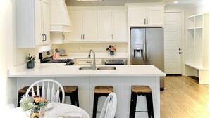 A modern kitchen with white cabinetry, a central island with stools, a stainless steel refrigerator, and a chandelier. - The Oaks, 3BR Escape by Velvet Ditch Villas (Oxford)