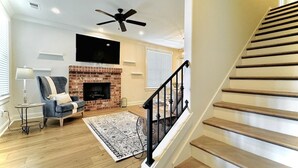 A living room with a fireplace, a sofa, a TV, and a staircase. - The Oaks, 3BR Escape by Velvet Ditch Villas (Oxford)