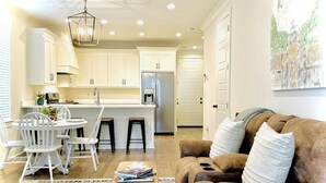 A modern kitchen with white cabinets, a stainless steel refrigerator, and a dining area with white chairs and a wooden table. - The Oaks, 3BR Escape by Velvet Ditch Villas (Oxford)