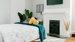 A bedroom with a bed, a TV mounted above a fireplace, and a large plant.