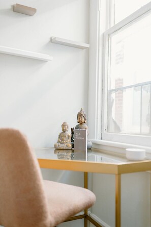 A minimalist room with a white wall, a small table with two Buddha statues, a sign reading "So, I Do Anything," and a window with a view of buildings. - Perch 𓆱 BnB, 3/1 + yoga rm in Victorian Dist East (Savannah)