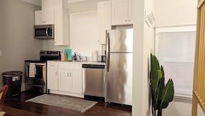 A modern kitchen with white cabinets, stainless steel appliances, and a wooden floor.