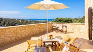 A terrace with a table, chairs, and an umbrella, overlooking a scenic landscape. - Villa Hara Faragi - Three Bedroom Villa, Sleeps 7 (Crete)