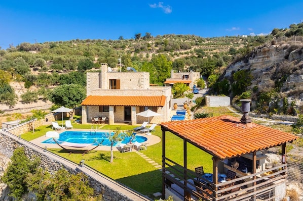 Una villa de piedra con piscina, mobiliario exterior y vistas a las colinas circundantes.