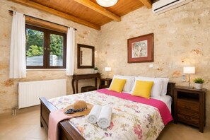Une chambre à coucher comprenant un lit, une table de chevet, une commode, une fenêtre avec des rideaux, un radiateur et un plafond en bois.
