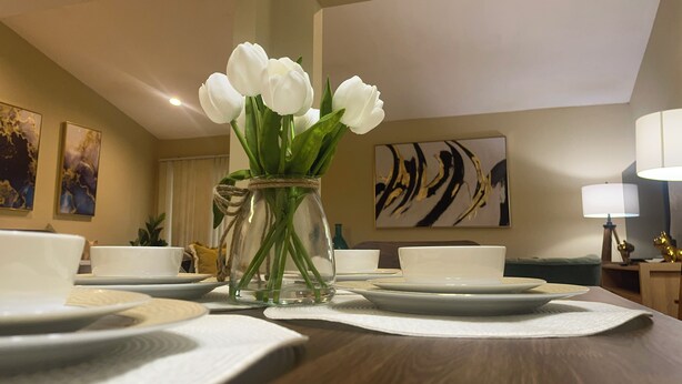 Una mesa de comedor con platos blancos y un florero de vidrio transparente con flores blancas.