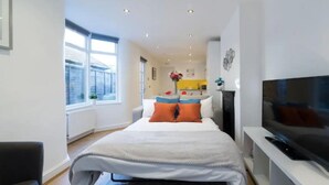 A modern bedroom with a bed, a TV, and a view of the kitchen. - Charming Tower Bridge House (London)