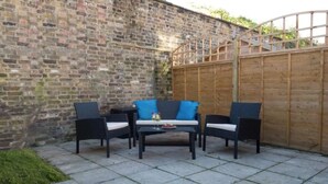 An outdoor patio with a brick wall, a wooden fence, and a table with chairs. - Charming Tower Bridge House (London)