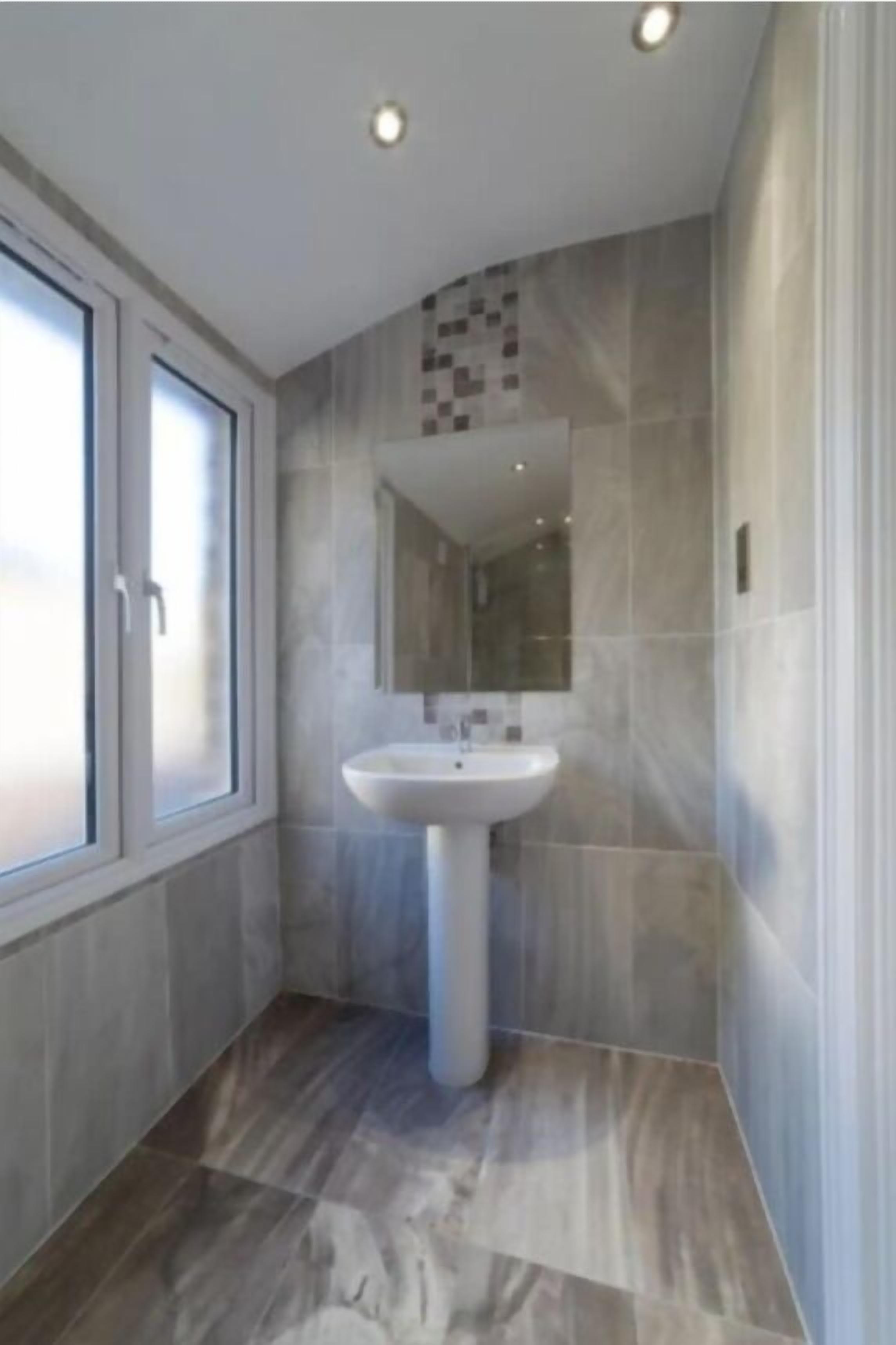 A modern bathroom with a pedestal sink, large mirror, and a window with frosted glass.