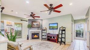 A living room with a fireplace, ceiling fans, a TV, and a dining area. - Beyond Blessed by Jackson Mountain Rentals (Pigeon Forge)