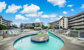 Un espace piscine doté de chaises longues, d’un élément décoratif central avec de l’eau et offrant une vue sur des immeubles à plusieurs étages en arrière-plan.