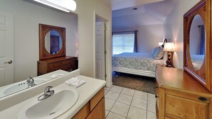 A hotel room with a large bathroom, a bed with patterned bedding, and a bedside lamp. - Beyond Blessed by Jackson Mountain Rentals (Pigeon Forge)