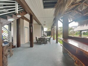 A covered outdoor area with a wooden bench, a table with chairs, and a staircase leading to an upper level. - Blue Moon by Ryson Vacation Rentals (Galveston)