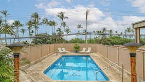 A rectangular pool with a tiled deck, surrounded by a fence and palm trees. - Island Surf 510A by Maui Rental Group (Kihei)