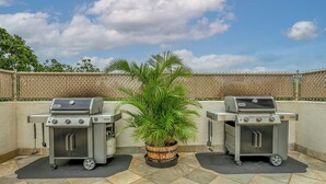Two portable grills on a patio with a potted plant in the center. - Island Surf 510A by Maui Rental Group (Kihei)