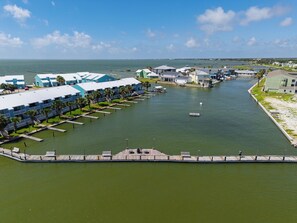 A marina with docked boats, a pier, and a row of blue buildings with balconies. - Kontiki Beach #221 by Miss Kitty’s (Rockport)