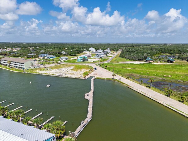 A waterfront property with a dock, a large building, and surrounding greenery. - Kontiki Beach #222 by Miss Kitty’s (Rockport)