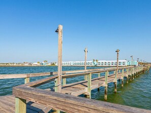 A wooden pier extending into calm water with a clear sky above. - Kontiki Beach #222 by Miss Kitty’s (Rockport)