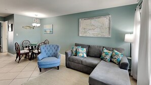 Ein Wohnzimmer mit grauem Sofa, blauem Sessel und einem Essbereich mit Stühlen und Tisch.