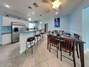 A modern kitchen with a central island, bar stools, and a dining table with chairs.