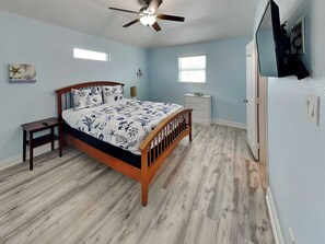 A bedroom with a bed, a nightstand, a dresser, a ceiling fan, and a window. - Our Shore Thing by Ryson Vacation Rentals (Galveston)