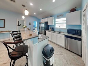 A modern kitchen with a central island, stainless steel appliances, and a view of the beach. - Our Shore Thing by Ryson Vacation Rentals (Galveston)