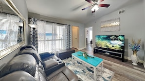 A modern living room with a leather sofa, a TV, and a decorative plant. - Glowing Fun by Ryson Vacation Rentals (Galveston)